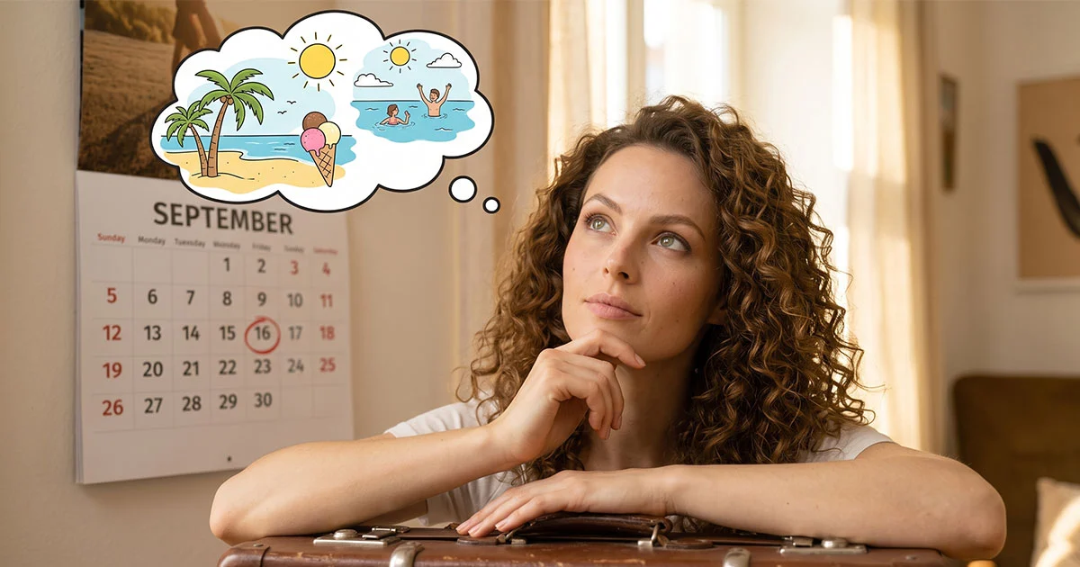 Una donna con capelli ricci appoggiata a una valigia guarda pensosa un calendario a muro sulla pagina di settembre con la data del 16 cerchiata, mentre immagina le vacanze estive al mare.