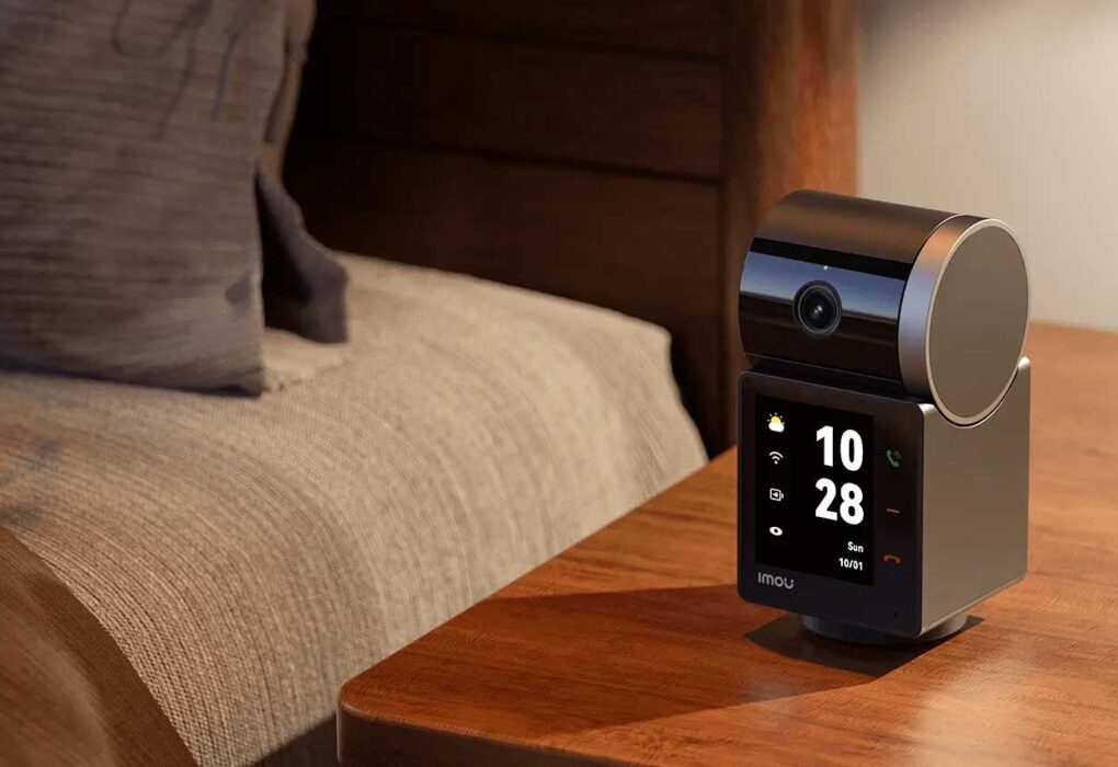 Telecamera smart Imou Rex VT Pro posizionata su un comodino in legno accanto al letto con display attivo che mostra orologio e tasti chiamata