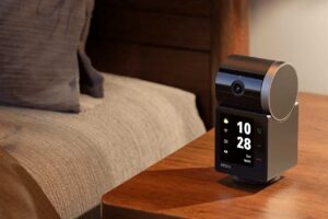 Telecamera smart Imou Rex VT Pro posizionata su un comodino in legno accanto al letto con display attivo che mostra orologio e tasti chiamata