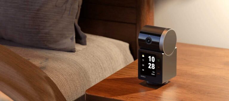 Telecamera smart Imou Rex VT Pro posizionata su un comodino in legno accanto al letto con display attivo che mostra orologio e tasti chiamata